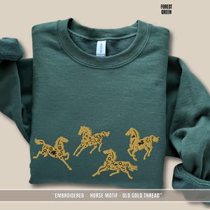 Flat lay of forest green sweatshirt showing detailed old gold & black horse embroidery stitching