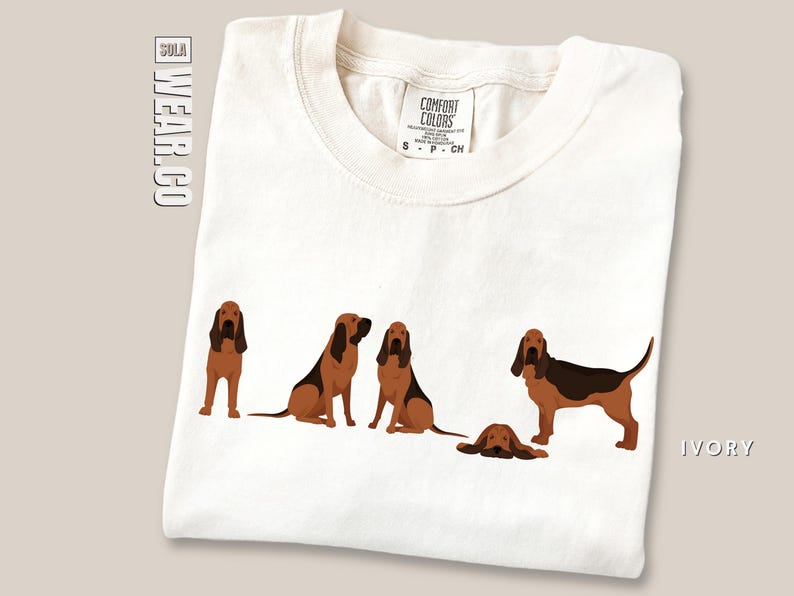 May include: A white t-shirt with a graphic of five brown and black Bloodhound dogs. The shirt is a Comfort Colors brand and is available in ivory.