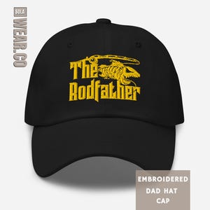 May include: Black dad hat with yellow embroidered text and graphic. The text reads "The Rodfather" with a fish skeleton design. The hat is a classic baseball cap style.
