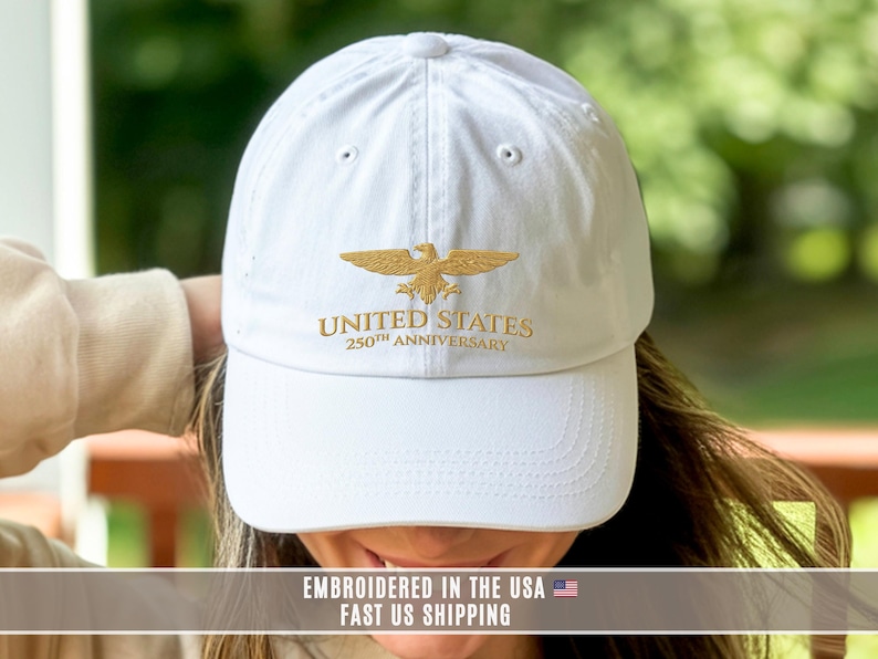 White embroidered United States 250th anniversary cap with gold eagle design, worn outdoors showing front stitching.
