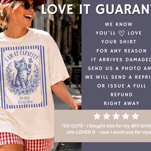 Sola Mio Co Love It Guarantee slide for the I Am at Capacity funny cat shirt, reassuring buyers that they can message with a photo if their graphic tee arrives damaged or with a print issue.