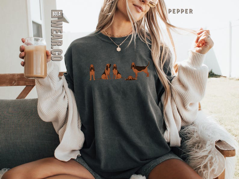 May include: A woman wearing a dark gray t-shirt with a graphic of four bloodhounds. The shirt has a distressed look and the graphic is in shades of brown and black.