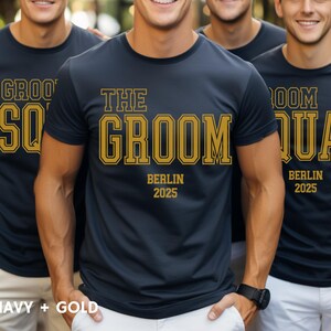 Peut inclure: Quatre t-shirts bleu marine avec des lettres dor&eacute;es. Les t-shirts disent "Groom Squad", "The Groom", "Groom Squad", et "Groom Squad". Les t-shirts ont &eacute;galement le texte "Berlin 2025" sur eux.