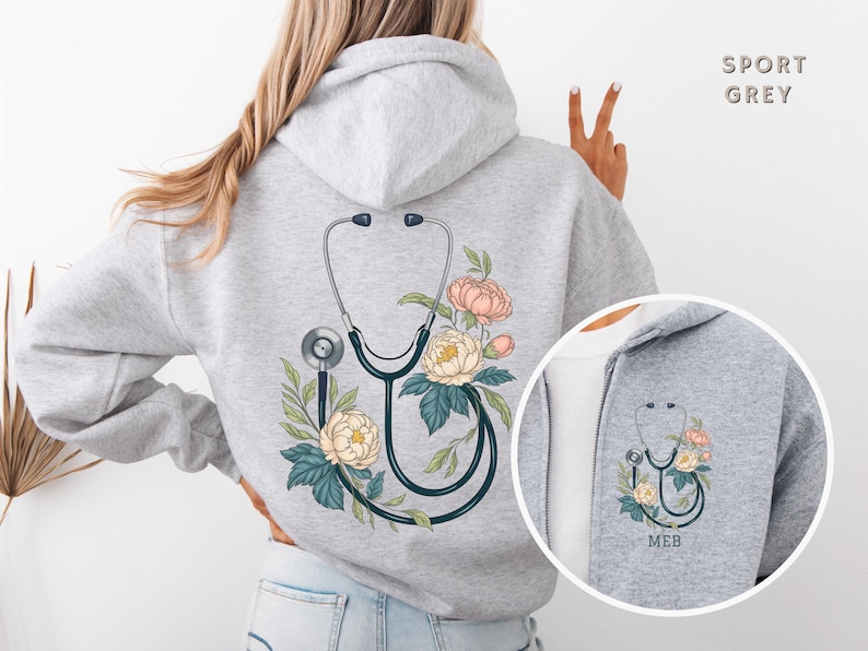 Pu&ograve; includere: Una felpa con cappuccio grigia con un design floreale e uno stetoscopio sul retro. La felpa &egrave; mostrata su un manichino. Il testo "Sport Grey" &egrave; visibile nell'angolo in alto a destra dell'immagine.