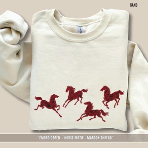 Beige Sand sweatshirt folded to show maroon embroidered horses across the chest