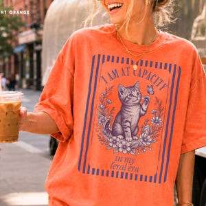 Feral Era Shirt on a Burnt Orange Comfort Colors tee featuring a cute vintage cat illustration and I Am at Capacity quote, styled as a funny oversized graphic tee for cat lovers, overstimulated women, introverts, and coffee run outfits.