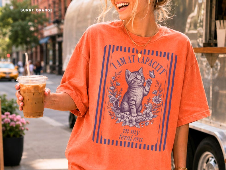 Feral Era Shirt on a Burnt Orange Comfort Colors tee featuring a cute vintage cat illustration and I Am at Capacity quote, styled as a funny oversized graphic tee for cat lovers, overstimulated women, introverts, and coffee run outfits.