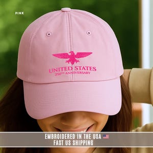 Pink embroidered United States 250th anniversary baseball cap with eagle design, casual lifestyle photo worn by model.