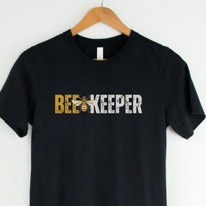May include: Black t-shirt with the text "BEEKEEPER" in white and yellow with a bee graphic in the middle of the text.