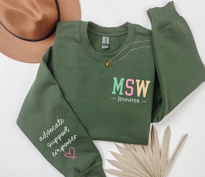 May include: Green sweatshirt with the text "MSW - JENNIFER -" on the front and the text "advocate support empower" on the left sleeve. The sweatshirt has a pink heart on the sleeve.