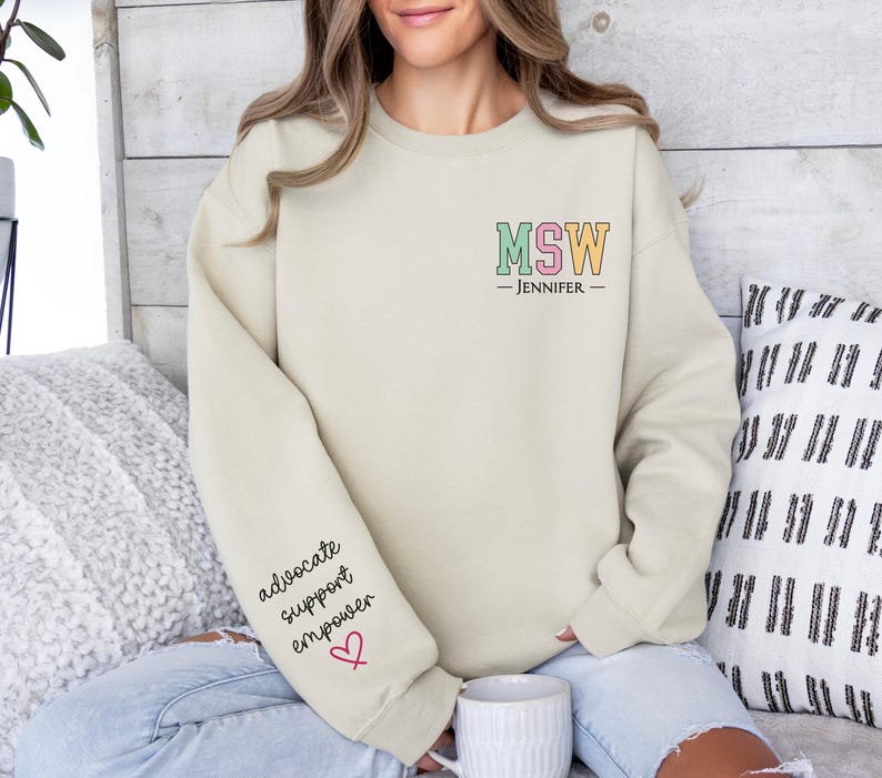 May include: A beige sweatshirt with the text "MSW - Jennifer" on the front and the words "advocate, support, empower" and a red heart on the left sleeve.