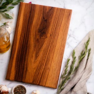 May include: A rectangular wooden cutting board with a rich brown color and visible wood grain. The board is surrounded by ingredients like rosemary, garlic, and peppercorns, suggesting a culinary theme. The board's dimensions are not visible.