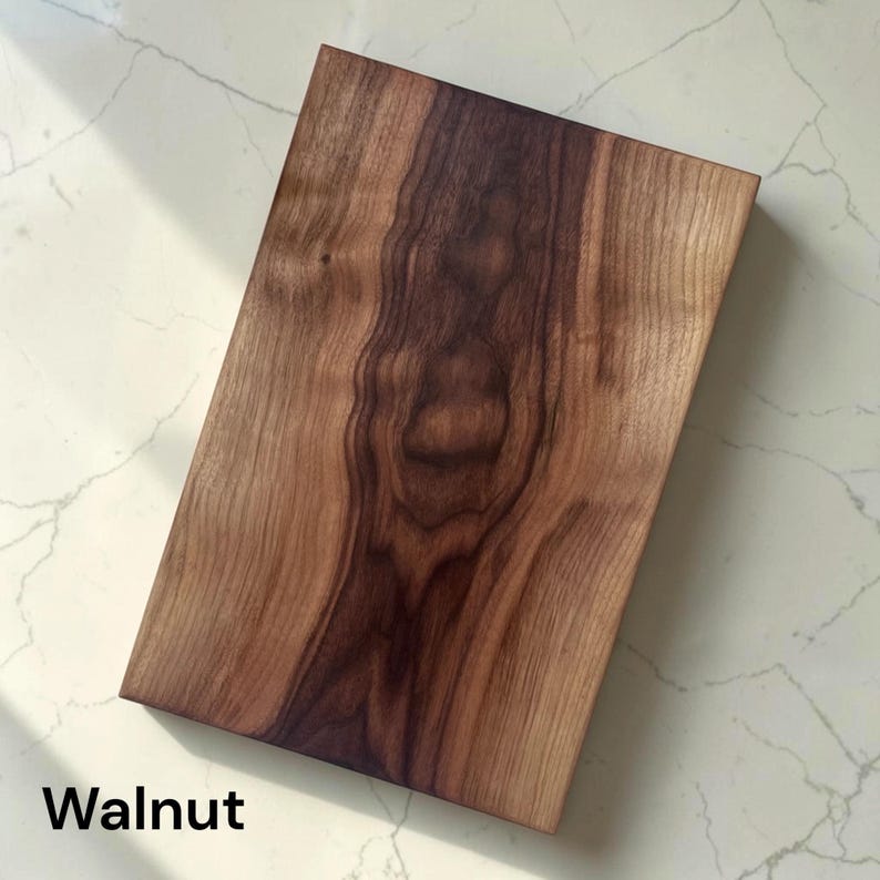 May include: A rectangular walnut wood cutting board featuring a prominent dark brown central grain pattern that transitions into lighter brown tones toward the edges. The surface displays natural wood swirls and organic lines throughout the piece.