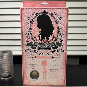 May include: A pink box with the text "Pally's Faces & Body" and a silhouette of a woman's profile. The box includes a diagram of a doll with labeled parts and a list of included items like face, head, and body.