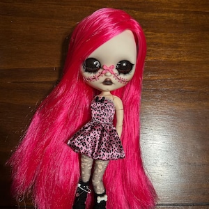 May include: A custom art doll with long, bright pink hair and a pale face with stitched details. The doll wears a pink leopard print dress, patterned stockings, and black boots. The doll's eyes are large and dark.
