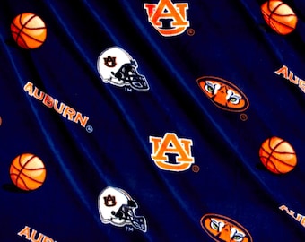 May include: Dark blue fabric with a repeating pattern of orange basketballs, the word "AUBURN", the letter "A" logo, and white and black football helmets. The fabric has a diagonal striped texture.