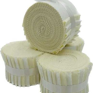 Puede incluir: Tres rollos de tela blanca, cada uno con una cinta blanca atada alrededor del centro. La tela está doblada en forma de espiral, creando un efecto de capas.