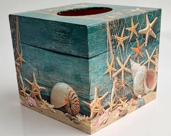 May include: A wooden tissue box cover with a nautical theme. The cover features a blue and green woodgrain background with starfish, seashells, and fishing nets.