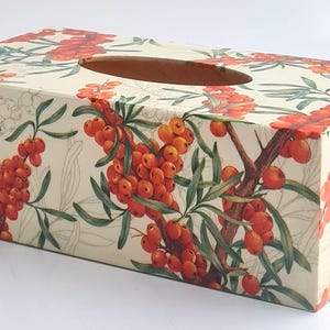 May include: Rectangular tissue box featuring a botanical design with orange berries and green leaves on a cream background. The box has an oval opening on top for tissue dispensing.