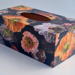 May include: A black tissue box cover with a floral design featuring large orange, pink, and purple flowers on a black background.