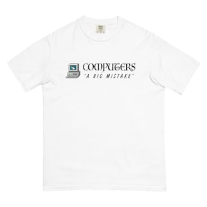 May include: A white short-sleeve t-shirt featuring a graphic of a vintage desktop computer icon followed by the black text "COMPUTERS" in a stylized font and the phrase "A BIG MISTAKE" in a smaller, sans-serif font centered on the chest.