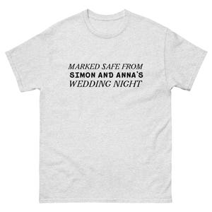 May include: A light gray t-shirt with the text "MARKED SAFE FROM SIMON AND ANNA'S WEDDING NIGHT" in black. The shirt has short sleeves and a crew neck.