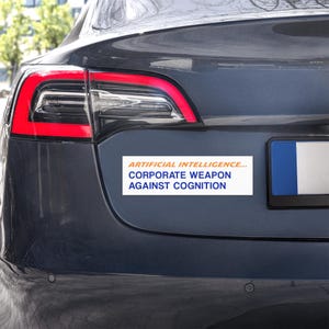 Pode incluir: Um autocolante retangular com fundo branco aplicado na bagageira de um veículo cinzento escuro. O autocolante apresenta o texto laranja ARTIFICIAL INTELLIGENCE... e o texto azul CORPORATE WEAPON AGAINST COGNITION numa fonte sem serifa.