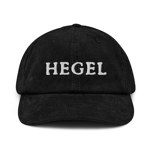 May include: Black corduroy baseball cap with the white embroidered word "HEGEL" across the front. The cap has a curved brim and an adjustable strap at the back.