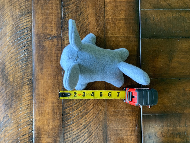 May include: A gray plush toy shaped like a small animal with large ears and a tail. The toy is measured with a yellow tape measure, showing it is 7 inches long.