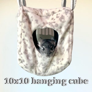 May include: A grey and white hanging cube pet bed with a small chinchilla inside. The cube is 25 cm by 25 cm.