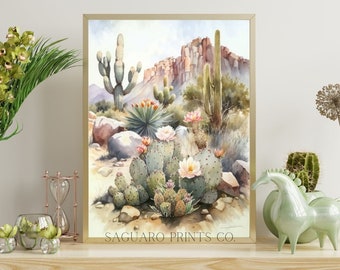 May include: A watercolor painting of a desert landscape with cacti, rocks, and flowers. The painting is framed in a gold frame and has the text "SAGUARO PRINTS CO." at the bottom.