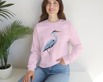 May include: A pink sweatshirt featuring a grey heron illustration on the front. The heron is standing on one leg with its head turned to the side. The sweatshirt has a relaxed fit and a crew neck.