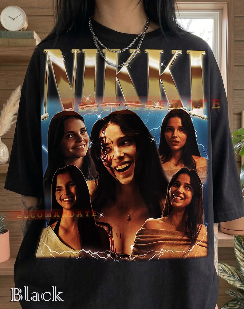 Może przedstawiać: Czarna koszulka z grafiką z napisem "NIKKI" w złotych metalicznych literach nad kolażem zdjęć kobiety. Obrazy są umieszczone na niebiesko-ż&oacute;łtym tle z błyskawicami. Słowo "Black" jest wydrukowane na dole.
