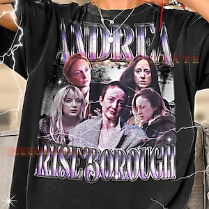 May include: Black t-shirt with a graphic featuring several women and the name "ANDREA RISEBOROUGH" in a vintage-style font. The design has a distressed appearance, with a faded colour palette and lightning bolt effects.