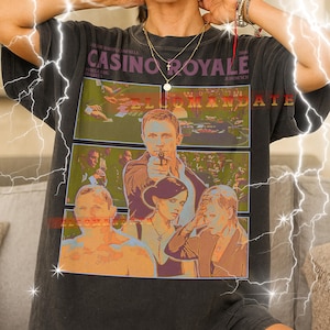 May include: Dark gray unisex t-shirt featuring a movie poster design for "Casino Royale." The graphic includes images of actors and the film's title. The shirt is a relaxed fit.