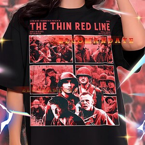 May include: Black unisex t-shirt featuring a graphic from the film "The Thin Red Line." The design includes a collage of images from the movie and the film's title in red. The shirt is oversized.