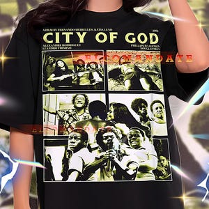 May include: Black oversized t-shirt featuring a movie poster design. The poster includes the title "CITY OF GOD" and various images from the film. The shirt is worn by a person.