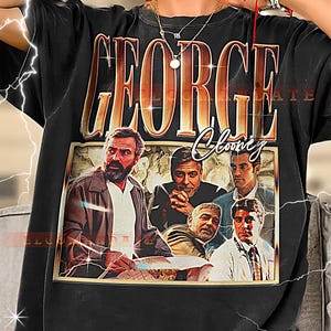 May include: Black t-shirt featuring a vintage-style graphic of George Clooney and the text "GEORGE Clooney" in gold lettering. The graphic includes multiple images of the actor. A stylish and comfortable tee for fans.
