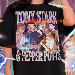 May include: Black graphic t-shirt featuring the text "TONY STARK & PEPPER POTTS" in a colorful, retro font. The shirt has a collage of images of characters from a movie. The model is wearing a 2XL shirt.