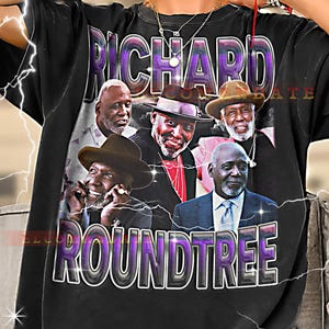 May include: Black t-shirt featuring a graphic of Richard Roundtree with the name in a purple and white design. The shirt displays multiple images of the actor. The word "RICHARD" is arched across the top, and "ROUNDTREE" is arched across the bottom.