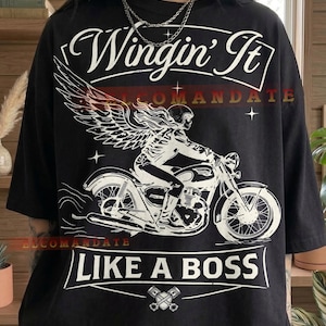May include: Black t-shirt with a white graphic of a skeleton riding a motorcycle with angel wings. The text "Wingin' It" is above the graphic, and "Like a Boss" is below. The word "Black" is at the bottom.