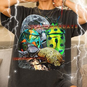 Könnte beinhalten: Dunkelgraues Unisex-T-Shirt mit einem farbenfrohen Käfer- und Vollmond-Motiv. Das Design enthält das Wort "DATE" in Rot. Das T-Shirt hat eine lockere Passform.