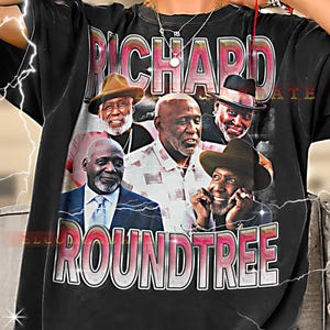 Pode incluir: T-shirt preto com um gráfico de Richard Roundtree e o texto "RICHARD ROUNDTREE" em rosa e branco. O gráfico inclui várias imagens do ator. A camisa é de estilo vintage.