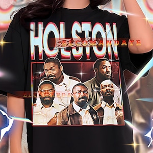May include: Black unisex t-shirt with the text "HOLSTON Becker ANDATE" in a retro font. The shirt features a graphic of six men in a rectangular frame. The model is wearing a 2XL shirt.