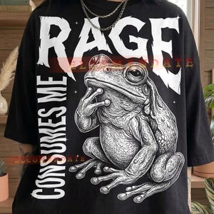 Könnte beinhalten: Schwarzes T-Shirt mit einer detaillierten Illustration einer Kröte und dem Text "RAGE CONSUMES ME" in Weiß. Die Kröte befindet sich in einer denkenden Pose. Das Wort "Black" steht unten auf dem T-Shirt.