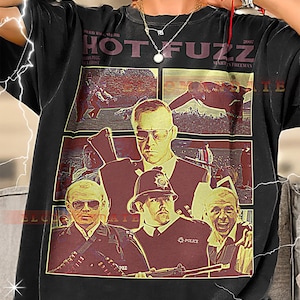 May include: Black t-shirt featuring a movie poster design for "Hot Fuzz" with multiple images of the cast. The shirt includes the movie title and the year 2007. The design is in shades of red, brown, and beige.