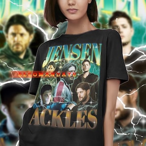 May include: Black t-shirt featuring a vintage-style graphic with the text "JENSEN ACKLES" in gold lettering. The design includes images of actors and the text "ELCOMANDATE". The shirt is worn by a person.