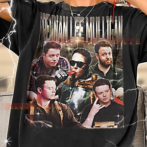 May include: Black t-shirt featuring a collage of images with the text "BRENNAN LEE MULLIGAN" in gold lettering. The collage includes multiple images of a person in various poses. The word "WELCOME" is also visible.