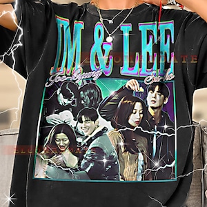 May include: Black graphic t-shirt featuring a group of people and the text "IM & LEE" in teal and pink. The shirt also has the names "Joo-kyung" and "Su-ho" in cursive. The design is a retro style.