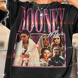 May include: Black t-shirt featuring a graphic of the name "ROONEY" in a pink, stylized font. Below the name is the name "Mara" in cursive. The graphic includes a photo of several women in a pink frame.